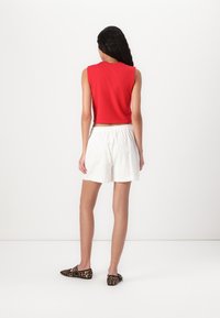 Rød kortermet topp uten ermer, hvite broderie anglaise-shorts og leopardmønstrede leiligheter. Enkelt design med elastisk liv på shortsene.
