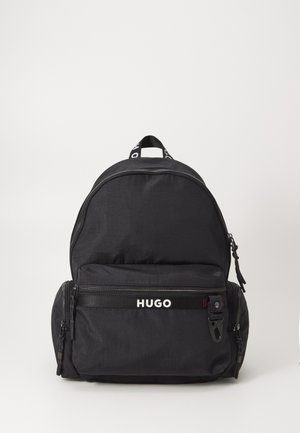 Black backpack made of nylon with a rounded shape. Features a front zip pocket, a logo band, and a top handle. Smooth texture.