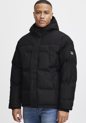 Chaqueta acolchada negra con capucha, con textura acolchada, bolsillos frontales y puños elásticos. Incluye un parche de logo en el lateral.