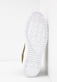 Semelle en caoutchouc blanche d'une chaussure marron, montrant des motifs géométriques de la bande de roulement avec des rainures et des sections texturées pour l’adhérence.