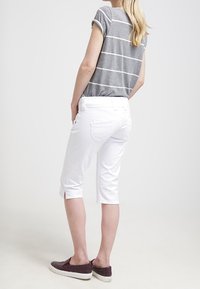 Lyhythihainen harmaa raidallinen paita, yhdistettynä valkoisiin capri-housuihin, luoden rentoa tyyliä. Kevyt kangas, jossa käännetyt hihat ja sivurei'ät.