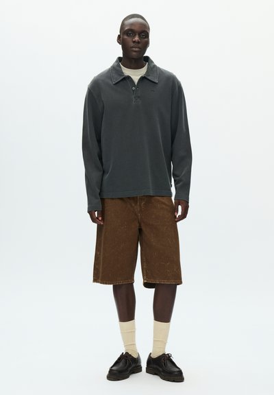 Dark gray long-sleeve polo with a collar, paired with brown knee-length shorts. Model wears beige socks and black shoes. Minimalist design.