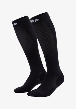 Black knee-length compression socks with ribbed texture, elastic cuff, and white logo detailing near the top and on the toe section.