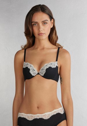 Soutien-gorge noir avec un accent en dentelle beige clair le long de l'encolure, bretelles ajustables et culotte noire assortie avec des accents en dentelle. Texture de tissu lisse.