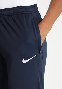 Marinblå Nike-joggers med elastisk midjeband, sidofickor och vit logodetalj på vänster lår, tillverkade av mjukt, lätt tyg.