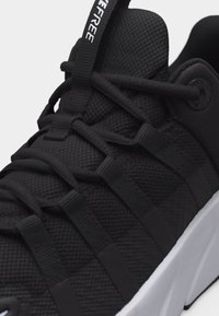 Μαύρο αθλητικό παπούτσι με υφή από διχτυωτό υλικό στην επάνω πλευρά, σύστημα κορδονιών με θηλιές, ετικέτα με λογότυπο και λευκή ενισχυμένη σόλα.