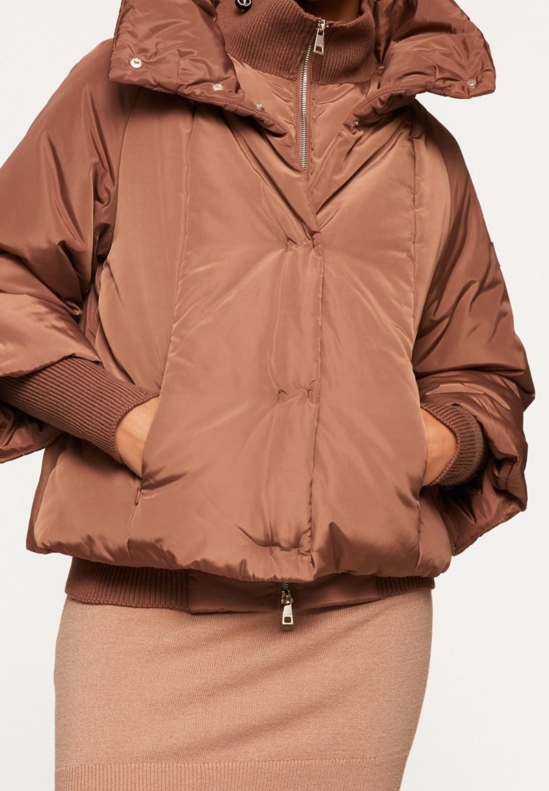 Ruskea pörrötakki, jossa on korkea kaulus, suuret hihat ja etutaskut. Sileä pinta, vetoketjusuljenta ja ribbireunat.