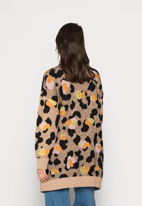 Sweter dziany w kolorze beżowym z kolorowym wzorem w cętki; posiada długie rękawy, ściągacze na mankietach oraz luźny krój.