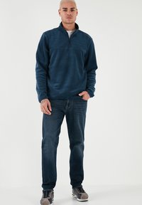 Pullover in pile blu navy con colletto a mezzo zip, abbinato a jeans in denim scuri e scarpe grigie con dettagli. Tessuto morbido, design casual.
