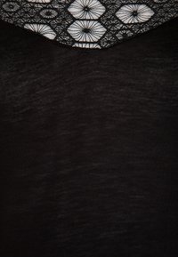 Mustapaita, jossa on yksityiskohtainen kuviollinen kaula-aukko, jossa on valkoisia kukkakuvioita ja geometrisia muotoja teksturoidun mustan taustan päällä.