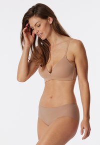 Nude nahtloser BH mit V-Ausschnitt und verstellbaren Trägern, kombiniert mit passenden Hipster-Unterhosen, beide aus glattem, dehnbarem Material hergestellt.