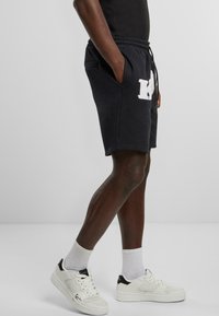 Dark gray cotton shorts with side pockets, elastic waistband, and a white embroidered logo. Worn with white sneakers and crew socks.