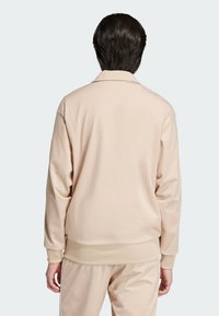 Light beige jacket with a smooth texture, featuring a collared neck, ribbed cuffs, and hem. Back view shows minimalistic design.