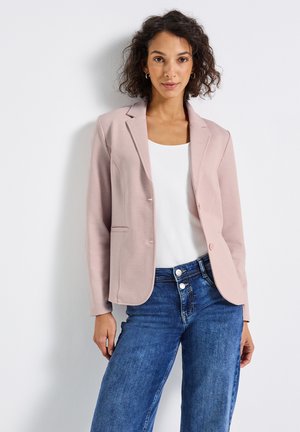 Světlý růžový blazer s dokonalým střihem, jednobuttonovým zapínáním a klopovými límci, v kombinaci s bílým topem a modrými džíny.
