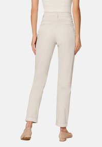 Beige rechte broek met een gladde textuur, twee achterzakken en opgerolde boorden. Gecombineerd met lichtgekleurde instapschoenen.