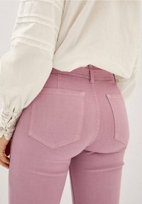 Różowe dżinsy o dopasowanym kroju, z dwiema tylnymi kieszeniami i średnim stanem, połączone z białą bluzką z długim rękawem z teksturowanymi rękawami.
