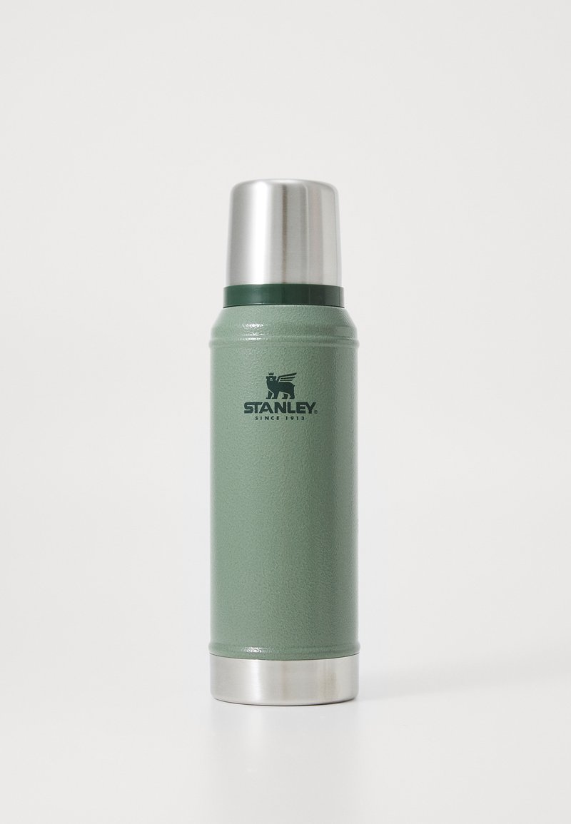 Termo de acero inoxidable verde con cuerpo texturizado, tapa plateada y un logotipo negro prominente. Forma cilíndrica diseñada para el aislamiento.