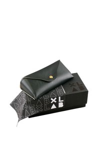 Portafoglio in pelle nera con chiusura a scatto dorata, posato su una scatola nera con motivi geometrici bianchi e un panno di pulizia nero.