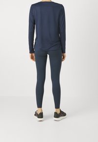 Granatowa bluzka z długim rękawem i legginsy wykonane z elastycznego materiału. Materiał o fakturze, dopasowany krój oraz czarne sportowe buty z kolorowymi akcentami.