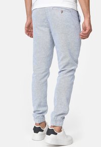 Pantalones jogger azul claro hechos de tela texturizada, pierna ajustada, puños elásticos, con bolsillos laterales y un detalle de botón en la parte trasera.