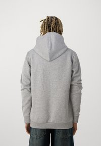 Sweatshirt à capuche gris avec des manches longues, en tissu doux, avec des poignets côtelés et une poche kangourou. L'arrière-plan est blanc uni.