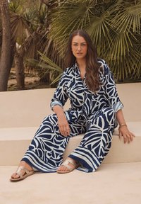 Conjunto de camisa y pantalones de patrón azul marino y azul claro con un corte relajado, combinado con sandalias metálicas. Tela suave y dos bolsillos frontales.