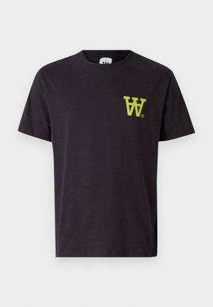 Svart bomull T-skjorte med neon-gul logo på brystet, kombinert med lyseblå denimbukser og svarte sko. Modellen står mot en hvit bakgrunn.