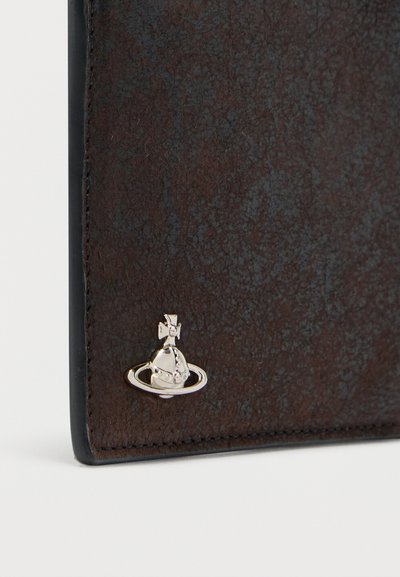 Γωνία πορτοφολιού από σκουρόχρωμο δερμάτινο ύφασμα με μικρό ασημένιο σφαιρικό έμβλημα και δακτύλιο προσαρτημένα κοντά στη ραμμένη άκρη.