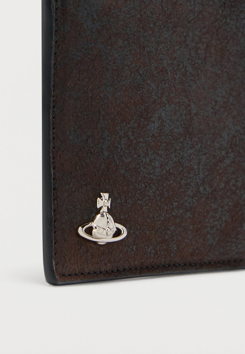 Angolo di portafoglio in pelle scura e strutturata con piccolo emblema a sfera d'argento e anello attaccato vicino al bordo cucito.