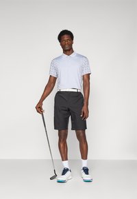 Svetlo modra polo majica s vzorcem, črne kratke hlače, bela pas in bele golfske čevlje z modrimi akcenti; golfer drži putter.