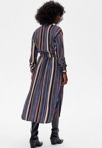 Pasiasta długa sukienka z pionowymi liniami w kolorze granatowym, beżowym i brązowym. Elastyczna talia, zapinane mankiety, zwiewna spódnica i czarne botki na wysokim obcasie.