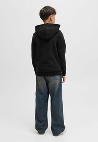 Felpa nera con cappuccio regolabile, abbinata a jeans oversize in denim azzurro chiaro. Il tessuto appare morbido, con una vestibilità comoda.