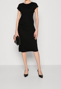 Czarna sukienka do kolan z krótkimi, podwiniętymi rękawami, z marszczonymi detalami po bokach. Połączona z czarnymi czółenkami o szpiczastej nosie i teksturowaną kopertówką.