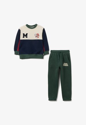 Sudadera de algodón con un diseño de bloques de color beige, azul marino y rojo, que presenta un logo "M" y un gráfico de Mario. Combinada con pantalones jogger verdes.