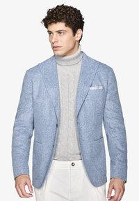 Blazer a zigzag blu chiaro con rever a punta, abbinato a un dolcevita grigio a trecce. Include due tasche frontali e una tasca sul petto.