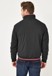 Schwarze Bomberjacke mit hohem Kragen und rot-weißen gestreiften Besätzen. Verfügt über eine glatte Oberfläche, elastische Bündchen und ein Logodesign am Kragen.