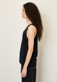 Juodas be rankovių marškinėlis su V formos iškirpte, pagamintas iš lengvos medžiagos, pasižymintis laisvu kirpimu, kuris šiek tiek gula žemiau juosmens.