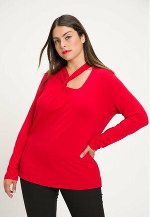 Red long-sleeve shirt with a knotted neckline detail and cut-out. Soft, stretchy fabric with a relaxed fit, paired with fitted black pants.