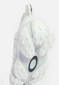 Weißer Sportschuh mit einem strukturierten Mesh-Obermaterial und einer Gummisohle, die mit erhabenen Punkten versehen ist. Enthält eine Lasche für einfachen Einstieg.