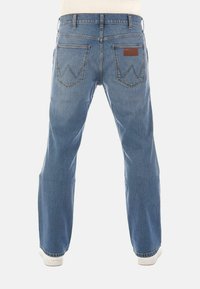 Jeans in denim azzurro chiaro con design a gamba dritta, dotati di una pettorina in pelle marrone e tasche posteriori distintive con cuciture a zig zag.