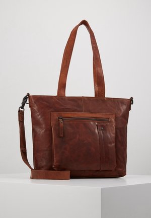 Bruine leren totebag met dubbele handvatten, voorvak met ritssluiting en afneembare schouderriem, geplaatst op een witte ondergrond.