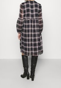 Mustat ruudulliset mekko pitkillä puffi-hihoilla, vyötäinen tiukasti muotoiltu ja laskeutuva hame, yhdistettynä polvipitkiin mustiin saappaisiin.