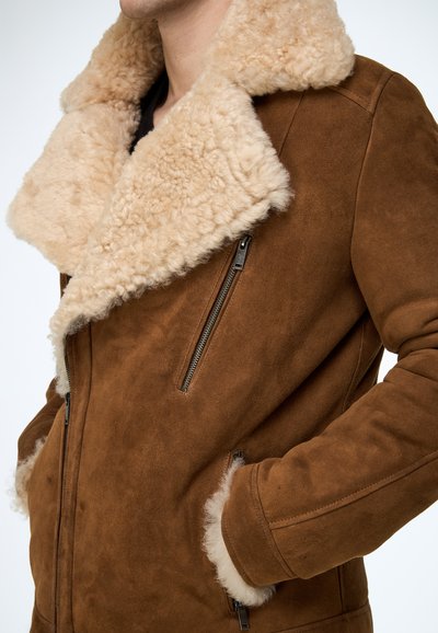 Braune Wildlederjacke mit großem, flauschigem beigefarbenem Schafsfellkragen. Verfügt über Reißverschlusstaschen und eine durchgehend weiche Textur.