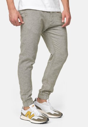 Pantalones jogger gris claro con un acabado texturizado, con piernas ajustadas y puños elásticos. Combinados con zapatillas blancas y grises.