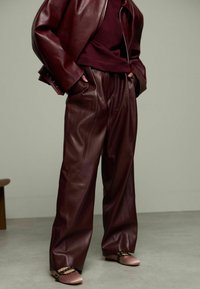 Veste en cuir bordeaux et pantalon en cuir ample associés à des ballerines rose clair avec des brides et des accents subtils en métal.