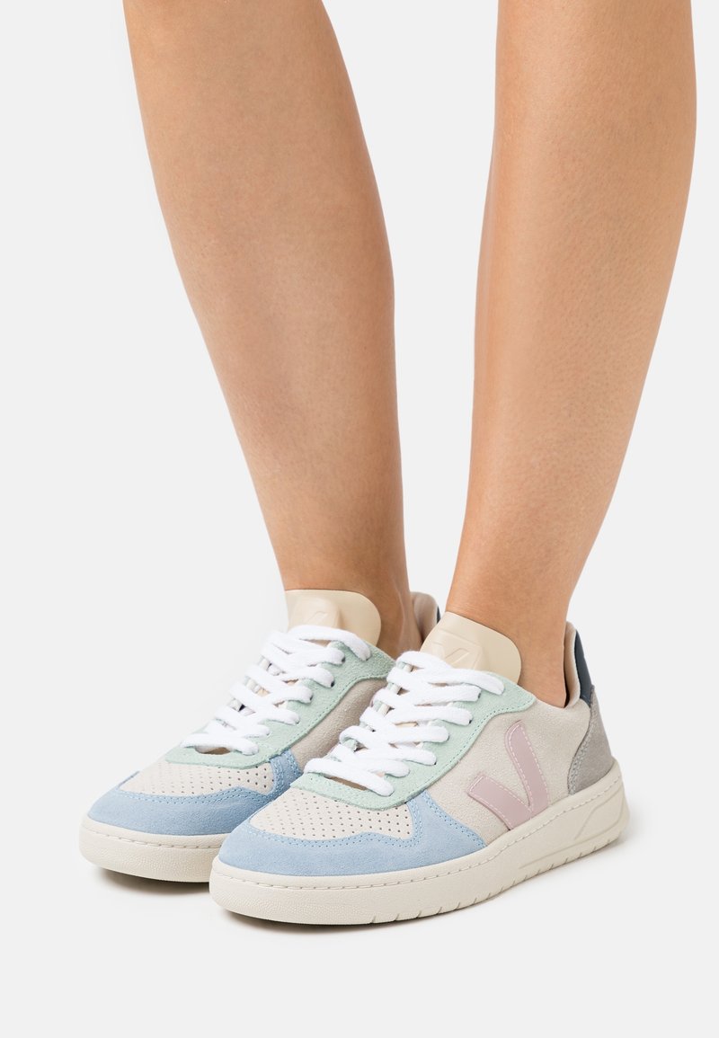 Baskets multicolores en daim bleu clair, vert, beige et gris avec un design perforé, des lacets blancs et un accent de logo rose.