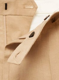 Tela beige con un acabado texturizado, que presenta herrajes negros y una cremallera visible. Incluye detalles de costura y una solapa abotonada.