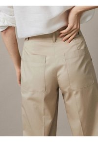 Pantalons beiges taille haute avec une texture lisse, deux poches arrière et un design à jambe droite. Les coutures sont soigneusement cousues.