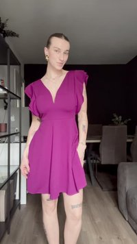 Tettsittende lilla kjole med volanger på korte ermer, dyp V-hals og utsvingt skjørt. Glatt stoff, knelengde, med definert midje.