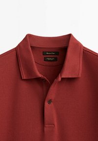 Polo en maille texturée à col, manches courtes, de couleur rouge foncé avec deux boutons et étiquettes de marque noires à l’intérieur de l’encolure.